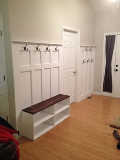 a room with white walls and wooden flooring has several coat racks on the wall