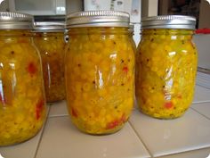 three jars filled with yellow food sitting on top of a white tile counter next to each other