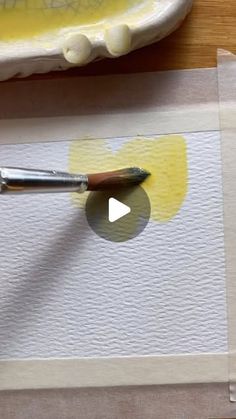 a person using a paintbrush to paint a piece of paper with yellow ink on it