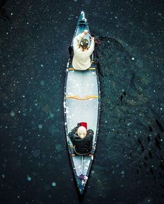 two people in a canoe on a body of water with snow falling all over the ground