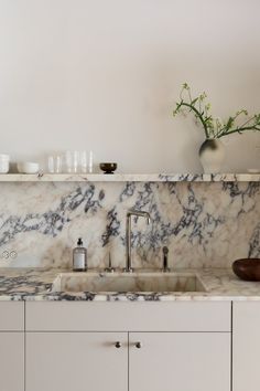 a kitchen with marble counter tops and white cupboards next to a vase filled with flowers