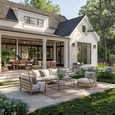 a white house with lots of windows and furniture in the front yard, surrounded by lush green grass