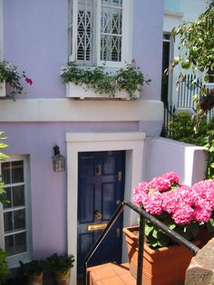 a purple house with potted plants and flowers on the front steps, next to a blue door