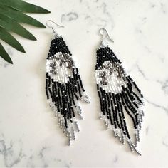 the black and white beaded earrings are hanging on a marble table next to a plant