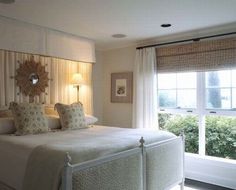 a large white bed sitting in a bedroom next to a window with curtains on it