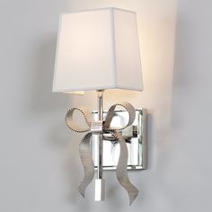 a wall light with a white shade on it and a silver ribbon around the lamp