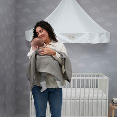 a woman holding a baby in her arms while standing next to a white crib