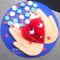 a hand holding a red heart on top of a blue plate with white and red flowers