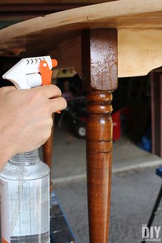 a person spray painting a wooden table with an orange and white sprayer on it