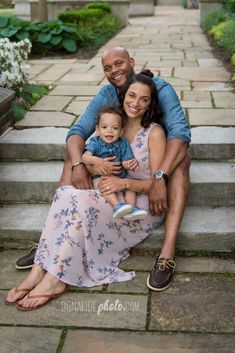 a man and woman are sitting on the steps with their baby in her lap, smiling at the camera