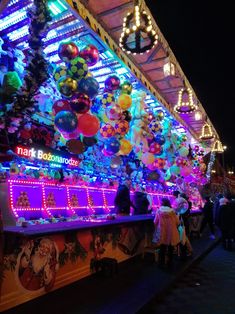 people are standing in front of a brightly lit food stand with balloons hanging from the roof