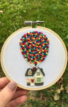 a hand holding up a small embroidery art piece with houses and a hot air balloon