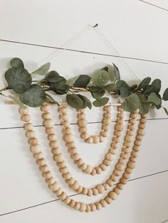 a wooden beaded garland with eucalyptus leaves and greenery hanging on a white wall