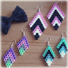 six pairs of beaded earrings are displayed on a wooden table next to a bow tie