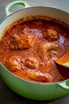 a green pot filled with meatballs and sauce on top of a wooden table next to a slice of bread