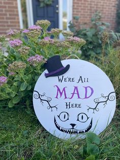 a sign that says we're all mad here in front of some plants and flowers