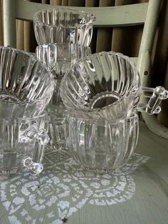 four glass dishes sitting on top of a table next to a chair with a curtain in the background