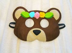 a brown bear mask with flowers on it's head is laying on a white sheet