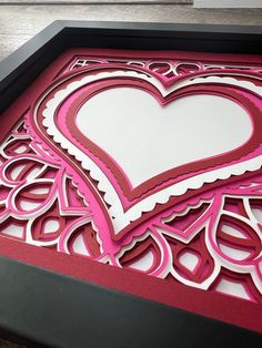 a pink and white heart cut out on a black framed paper with red trim around the edges