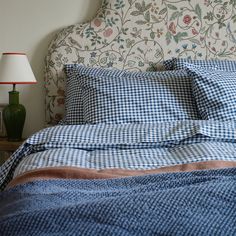 a bed with blue and white checkered sheets, pillows and a lamp on the nightstand