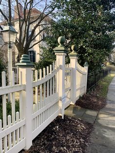 a white picket fence in front of a house with trees on the side walk way