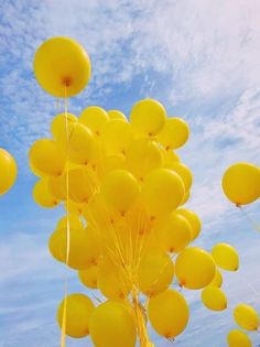 a bunch of yellow balloons floating in the air with blue sky and clouds behind them