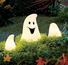 two white ghost statues sitting in the middle of some bushes with leaves around them and one is smiling