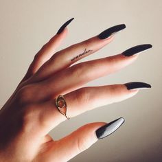 a woman's hand with black and white nail polish on it, holding a gold ring