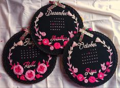 three embroidered calendars with pink flowers on them sitting on a white cloth covered surface