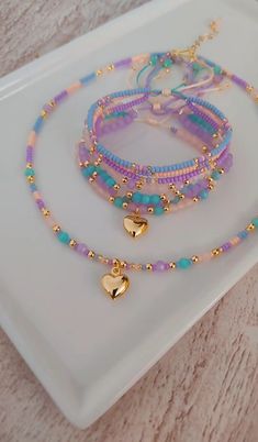 three bracelets with gold heart charms on a white plate next to pink and blue beads