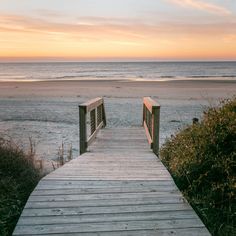 a wooden walkway leading to the beach at sunset