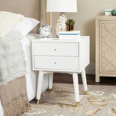 a white nightstand with a clock on it next to a night stand and a lamp