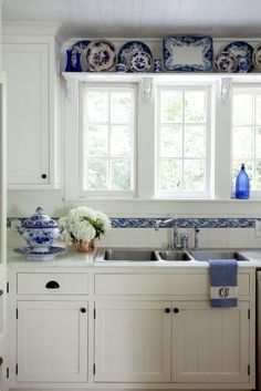 a white kitchen with blue and white decor on the window sill above the sink