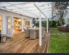 an outdoor patio with wooden floors and white pergolated roof over the dining area