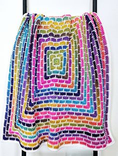 a multicolored crocheted blanket hanging on a wall next to a chair