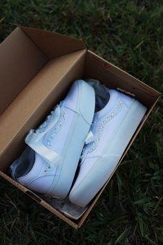 a pair of white sneakers in a box on the grass, with one shoe missing