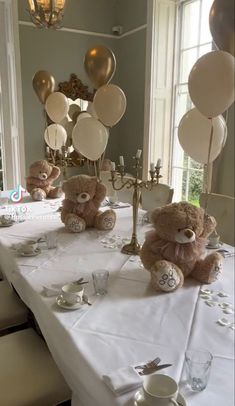 two teddy bears sitting at a long table with balloons and confetti on it