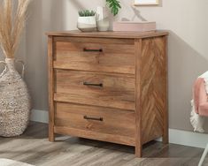 a wooden chest of drawers in a room with a pink chair and potted plant