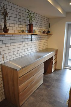 an empty kitchen with white brick walls and wooden cabinets, plants on the ledges