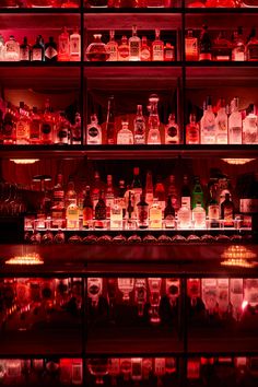 many bottles are lined up on shelves in a liquor store with red light coming from them