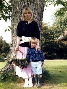 a woman standing next to a little boy in front of a tree