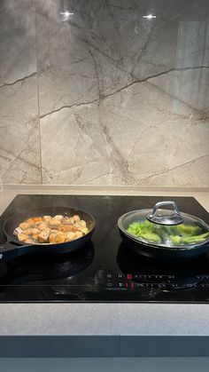 two pans with food cooking on top of a gas stove in front of a marble backsplash