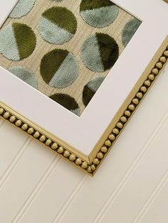 a close up of a framed art piece on a wall with white and gold trim