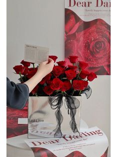 a person holding a bouquet of red roses in front of a book on a table