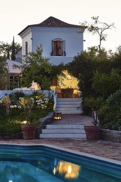 an outdoor swimming pool with steps leading up to the house and surrounding trees, shrubs, and plants