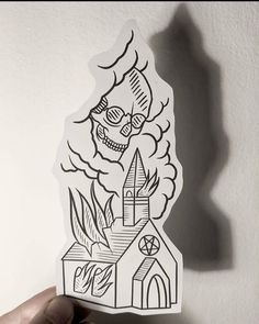 a hand holding up a sticker with a drawing of a church and skull on it