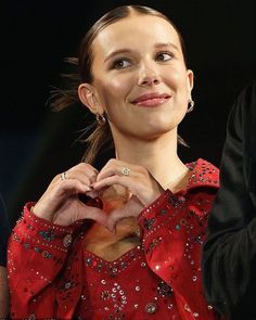 a woman in a red dress making a heart shape with her hands while standing next to a man