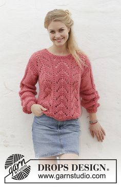 a woman standing next to a white wall wearing a pink sweater and denim skirt with her hands in her pockets