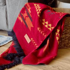 a red blanket sitting on top of a wooden floor next to a basket filled with pillows