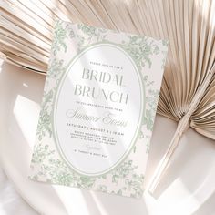 a white and green bridal brunch card on a plate with fan in the background